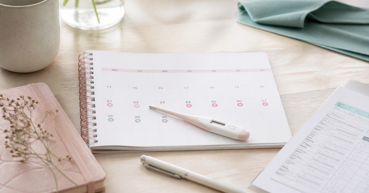 Zykluskalender mit markierter zweiter Zyklushälfte, Thermometer und Laborformular auf einem hellen Schreibtisch